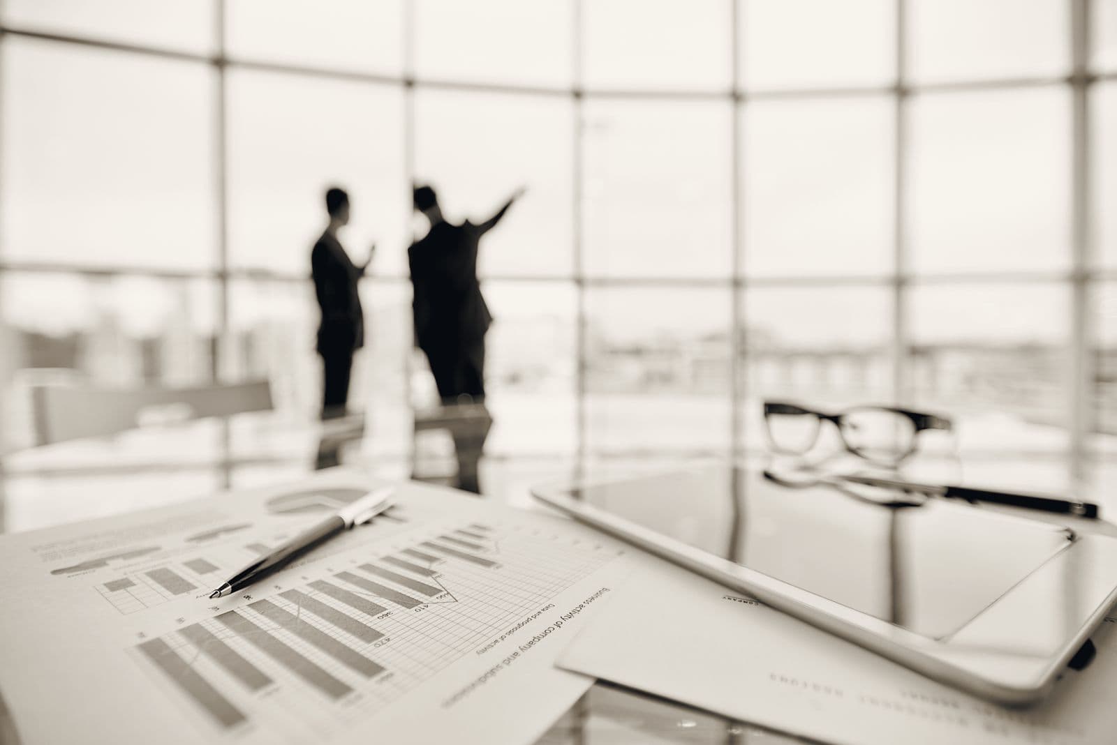 Two advisers in conversation by a window, with business planning documents in the foreground.
